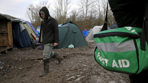 Un inmigrante pasa junto a un médico voluntario que presta servicio  en el campamento provisional para refugiados de procedentes de Irak, Kurdistán, Irán y Siria, cerca de Dunkerque (Francia). REUTERS / Pascal Rossignol