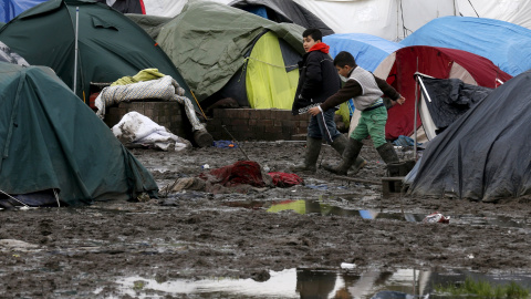 Dos niños inmigrantes caminan por el suelo enfangado entre las tiendas del  campamento provisional para refugiados de procedentes de Irak, Kurdistán, Irán y Siria, cerca de Dunkerque (Francia). REUTERS / Pascal Rossignol