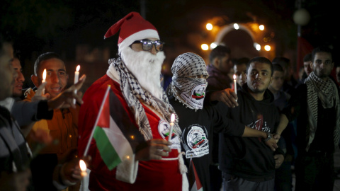 Palestinos enmascarados junto a un hombre  vestido de Papá Noel sostienen velas durante un acto para rendir homenaje a los palestinos asesinados recientemente por las tropas israelíes, el día de Navidad en Gaza.- REUTERS/Suhaib Salem
