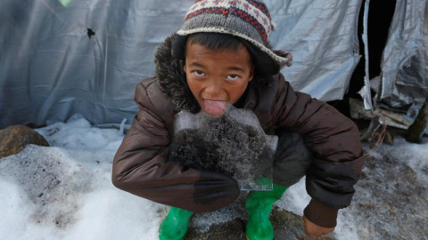 Un niño come un trozo de hielo delante de su refugio temporal en Laprak, en el distrito de Gorkha (Nepal). EFE/Narendra Shrestha