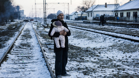 Un hombre sostiene a su bebé mientras espera con otros inmigrantes y refugiados en una estación de tren a un tren en el sur de Presevo en Serbia, 20 de enero 2016./AFP