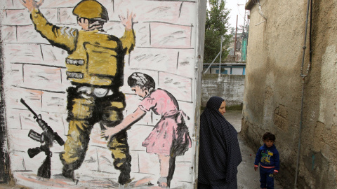 Una mujer palestina se encuentra con un niño en un callejón junto a la reproducción de un mural del artista callejero británico Banksy en al-Aroub campo de refugiados palestinos, al norte de la ciudad cisjordana de Hebrón. HAZEM BADER/AFP