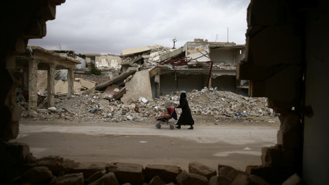Una mujer pasea con su bebé por las ruinas de la ciudad sitiada de Douma, al este de Damasco. - REUTERS