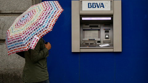 Una mujer con paraguas pasa junto a una oficina de BBVA  en Madrid. REUTERS/Andrea Comas