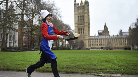 Una parlamentaria corre mientras da la vuelta a una tortita por los jardines de Victoria junto a las Casas del Parlamento en Londres, durante la tradicional carrera de tortitas para recaudar dinero para obras de caridad. EFE/Andy Rain