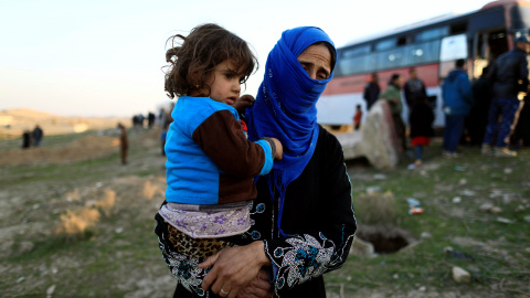 Una mujer, que acaba de huir de una aldea controlada por los militantes del Estado islámico, sostiene a su hija mientras se encuentra frente a un autobús antes de dirigirse al campamento de Hammam Ali, al sur de Mosul, Irak. REUTERS/Zohra B