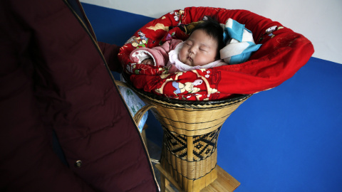 Una niña de 3 meses de edad se ve junto a su padre, envuelta en mantas en una cesta en una fiesta de bodas Tujia étnica tradicional durante se celebran el Año Nuevo Lunar en la ciudad Ziqiu, condado Changyang de la provincia china de Hubei,