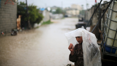 Un niño palestino se cubre la cabeza con una lámina de plástico en un día lluvioso en Khan Younis, al sur de la Franja de Gaza. REUTERS/Ibraheem Abu Mustafa