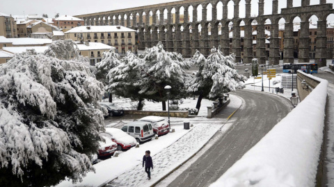 Una mujer camina por una calle junto al Acueducto de Segovia, que despertó hoy con una capa de más de diez centímetros de nieve. EFE/Aurelio Martín
