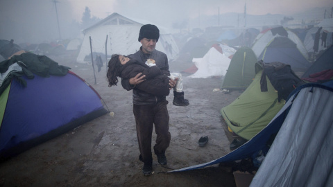 Un hombre lleva su hija en brazos sobre el barro tras las fuertes lluvias caidas durante la noche en una fría mañana en el campo de refugiados .- EFE