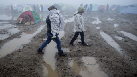 Un hombre lleva su hija en brazos sobre el barro tras las fuertes lluvias caidas durante la noche en una fría mañana en el campo de refugiados .- EFE
