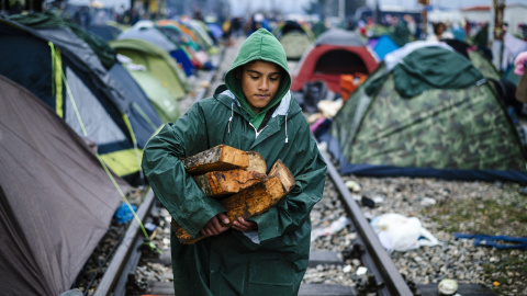 Un niño lleva leña bajo la lluvia en un campamento improvisado en la frontera entre Grecia y Macedonia, cerca de la localidad griega de Idomeni, donde miles de refugiados y migrantes están varados por el bloqueo de la frontera de los Balcan