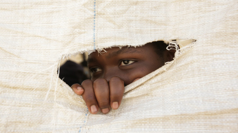 Una estudiante de secundaria mira a través de un agujero de un saco utilizado en una de las aulas improvisadas debido a la falta de instalaciones adecuadas en el colegio Eastview en Calcedonia, Harare (Zimbabue). EFE/Aaron Ufumeli