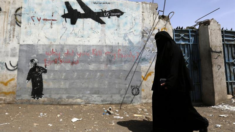 Una mujer camina junto a unas pintadas en contra de los drones estadounidenses y los ataques de Estados Unidos contra supuestas pociones de Al-Qaeda en Saná, Yemen. EFE/Yahya Arhab