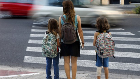 Una madre y sus hijas esperan a que los coches pasen para poder cruzar cuando van de camino a la escuela./ EFE-Archivo