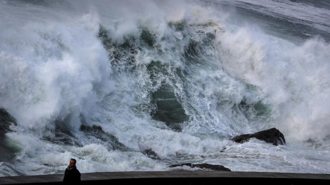 Un hombre pasea este domingo ajeno a una gran ola a punto de romper en el Paseo Nuevo de San Sebastián. EFE