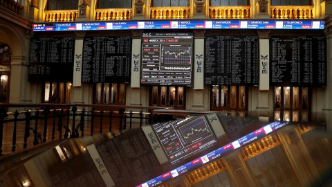 Una pantalla (al fondo) muestra un gráfico con la evolución del IBEX 35 en la Bolsa el pasado lunes. - EFE