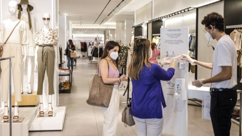 Dos clientas se desinfectan las manos con gel hidroalcohólico a la entrada de una tienda de ropa en Valencia.| Rober Solsona. Europa Press