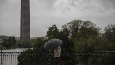 Un hombre protegido con un paraguas camina por el puente de Triana durante la alerta amarilla por tormentas en Sevilla. María José López / Europa Press / Archivo
