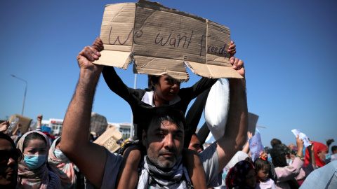 Un hombre sujeta a un niño durante las protestas pidiendo soluciones tras el incendio del campo de refugiados en Moria, Lesbos. / REUTERS