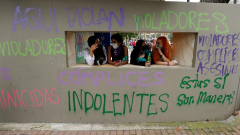 Varias mujeres conversan frente a una pared con grafitis pintados en las paredes de un Comando de Atención Inmediata (CAI) de la Policía durante unas protestas en Bogotá (Colombia).