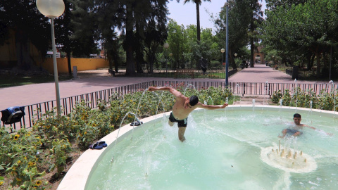 Dos jóvenes se refrescan en una fuente en el Jardín del Malecón de Murcia.