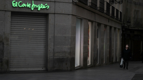 Una mujer con mascarilla pasa por delante de una tienda de El Corte Inglés en el centro de Madrid, cerrada durante el confinamiento decretado en marzo de 2020 por la pandemia del coronavirus. REUTERS/Susana Vera