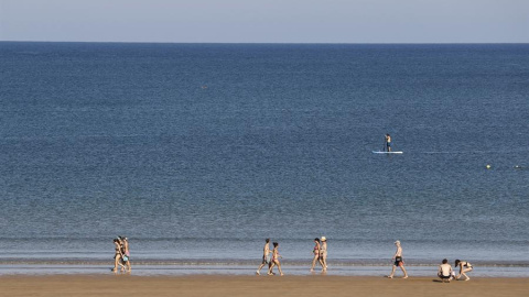 Veraneantes pasean por la playa ante un paddle surf en la localidad vizcaína de Plentzia, donde una joven ha denunciado haber sufrido una agresión sexual.