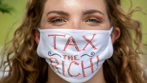 Una activista con una mascarilla en la que lleva escrito el lema "Tax the rich" ("Impuestos para los ricos"). REUTERS/Nick Iwanyshyn