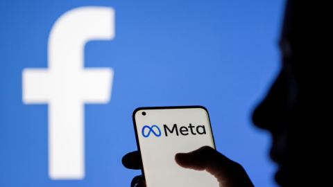 Una mujer sostiene un teléfono inteligente con el logotipo de Meta delante de la imagen de Facebook, a 28 de octubre de 2021.
