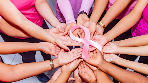 Mujeres sujetando un lazo rosa, símbolo de la lucha contra el cáncer de mama.