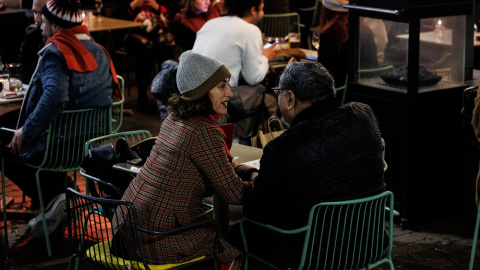 Dos personas en una terraza en la Plaza de Santa Ana para celebrar la llegada de la Nochebuena, a 24 de diciembre de 2021, en Madrid (España). A pesar de las nuevas restricciones, como el uso de la mascarilla en exteriores, que entra en vig