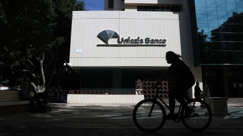 Una mujer en bicicleta pasa por las inmediaciones de la sede de Unicaja Banco en Málaga. E.P./Álex Zea