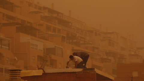 Unas personas trabajan en Aguadulce, Roquetas de Mar (Almería), que ha amanecido este martes bajo los efectos de una intensa calima.