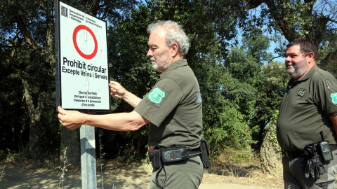 Agents Rurals desplegant un dels cartells que impedeix el pas per dins del massís de les Gavarres arran de l'entrada en nivell 3 del Pla Alfa.