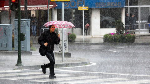 Una mujer pasa esta mañana por una calle de Compostela, enfrentándose a fuertes lluvias y a un intenso viento de una profunda borrasca procedente del Atlántico.