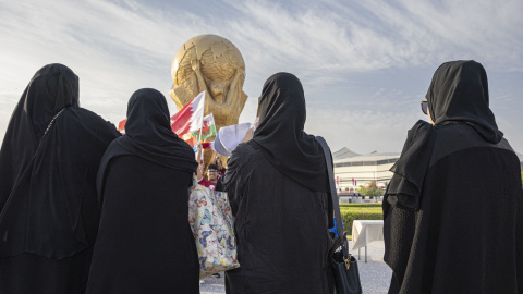 Mujeres en Catar con una recreación gigante de la Copa del Mundo al fondo.