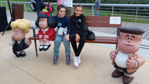 Dues nenes assegudes al costat de la nova escultura de Mafalda, a Santa Coloma de Gramenet.