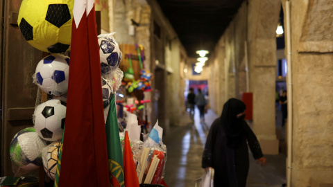 Una mujer camina, con el hiyab, por una calle de Catar decorada con banderas por el Mundial.