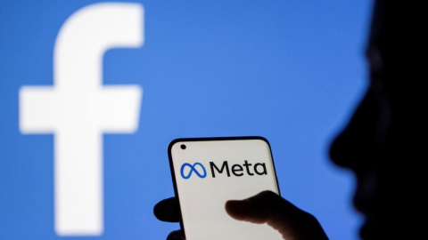 Una mujer sostiene un teléfono inteligente con el logotipo de Meta delante de la imagen de Facebook, a 28 de octubre de 2021.
