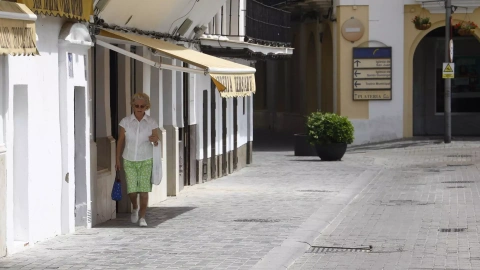 Una mujer intenta caminar por la sombra de los toldos por la calle debido a las altas temperaturas que se están registrando inusuales para el mes de abril, este viernes en Sevilla.