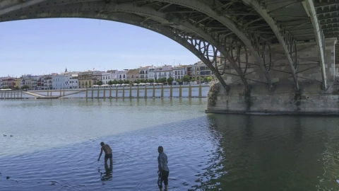 Dos personas se refrescan bajo el Puente de Triana, en Sevilla, donde este jueves se esperan temperaturas máximas de 37 grados, a 15 de junio de 2023