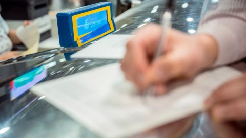 Una persona rellena unos documentos tras solicitar el voto por correo en el Edificio de correos, a 14 de junio de 2023, en Madrid.