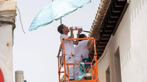 Unos trabajadores se cubren del sol con una sombrilla y beben agua en Granada, a 11 de julio de 2023.