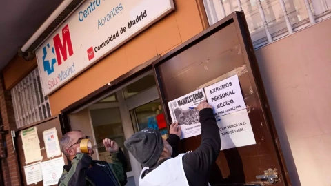 Dos hombres pegan carteles en la puerta del Centro de Salud de Abrantes, a 16 de febrero de 2023, en Madrid.