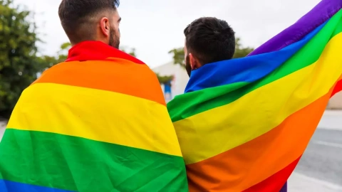 Una pareja de hombres LGTBI+ porta la bandera del colectivo.