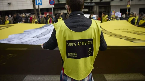Varias personas portan una banderola amarilla gigante de Amnistía Internacional en una manifestación, a 13 de febrero de 2022, en Madrid.