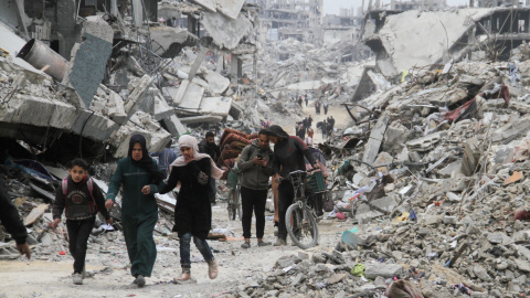 Palestinos caminan entre casas y edificios devastados.
