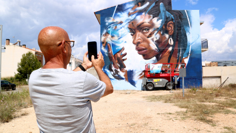 Un veí de l'Ametlla de Mar fa una foto al mural de l'artista Filite sobre Yemayá, patrona dels pescadors de Brasil Un veí de l'Ametlla de Mar fa una foto al mural de l'artista Filite sobre Yemayá, patrona dels pescadors de Brasil