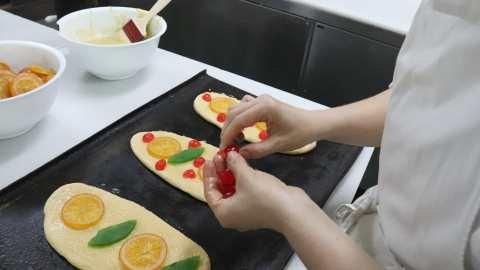 Una pastissera posa fruita confitada a les coques de Sant Joan en preparació Una pastissera posa fruita confitada a les coques de Sant Joan en preparació